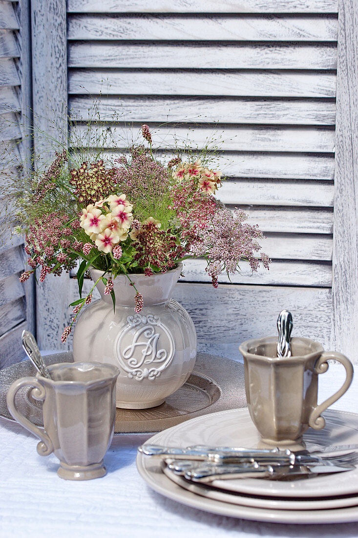 Jug of wild carrot 'Dara' flowers, place setting with mugs and silver cutlery