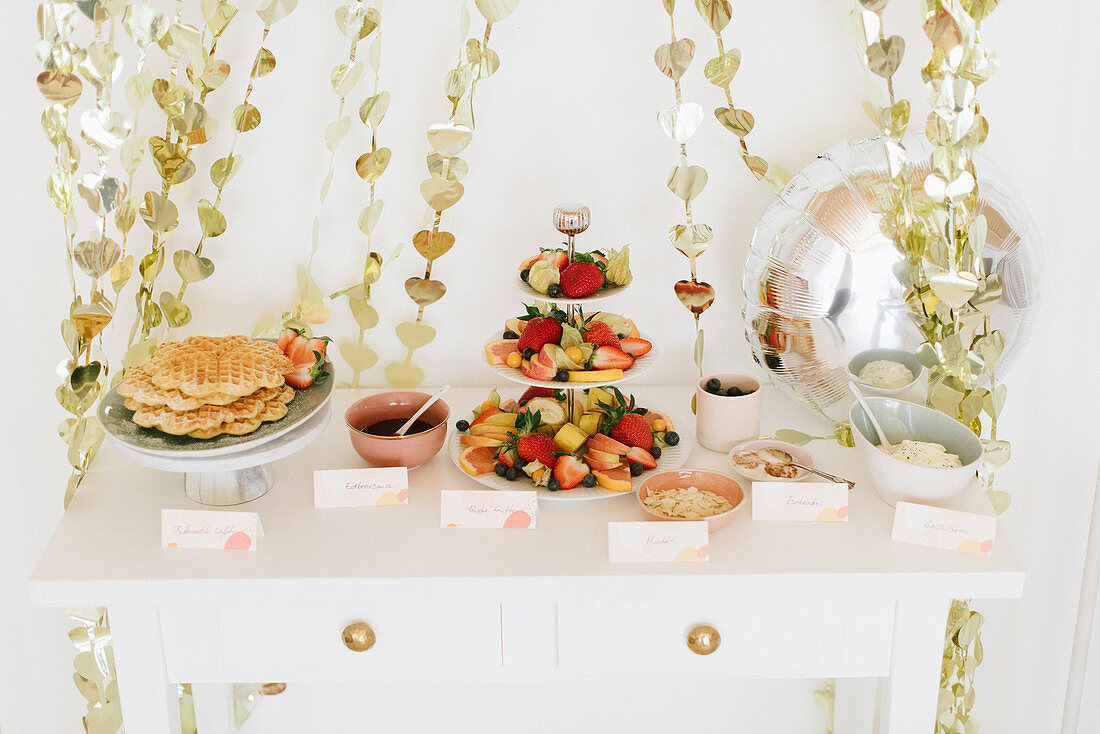 Waffles and fruits on party buffet table and garlands of shiny hearts