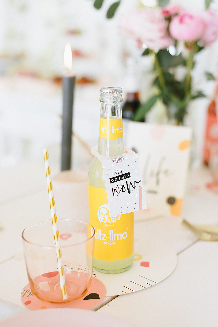 Limonadenflasche und Glas mit Strohhalm auf festlich gedecktem Tisch