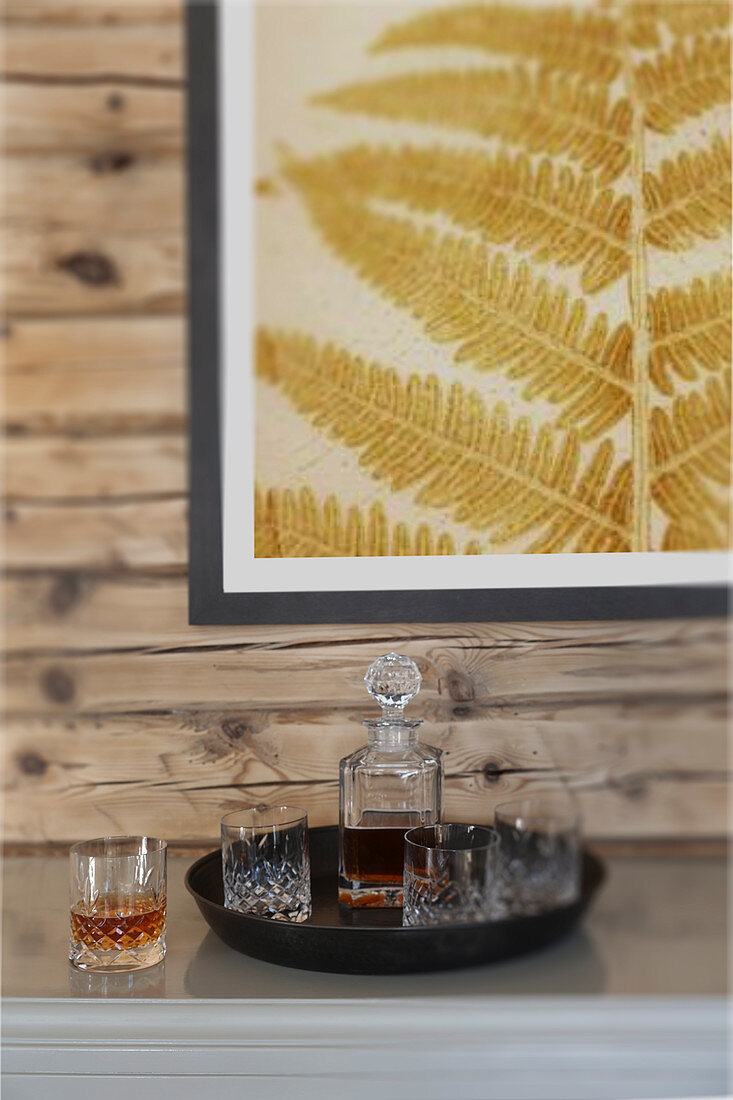 Tablett mit Karaffe und Whiskey-Gläsern unterm Bild mit Farnblatt