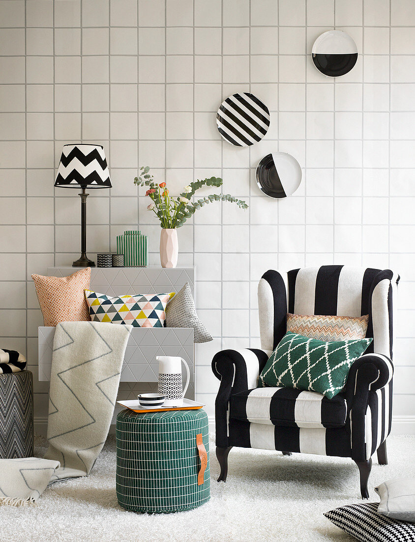 Grafisches Design: Sessel mit schwarz-weißem Bezug, Hocker, Regal, Kissen, Wandteller und Tapete in Fliesen-Look