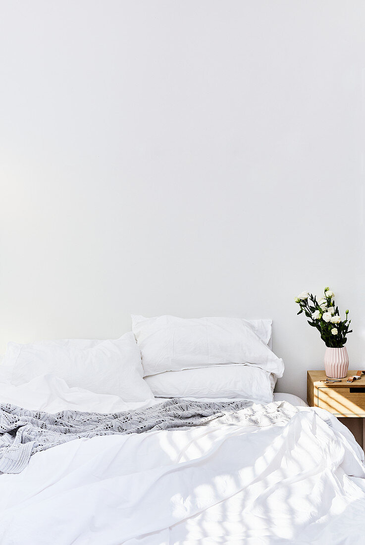 Sonnenlicht auf dem Bett im schlichten weißen Schlafzimmer