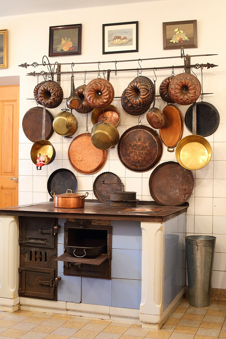 Collection of old pans and cake tins on wall above old wood-fired stove in kitchen