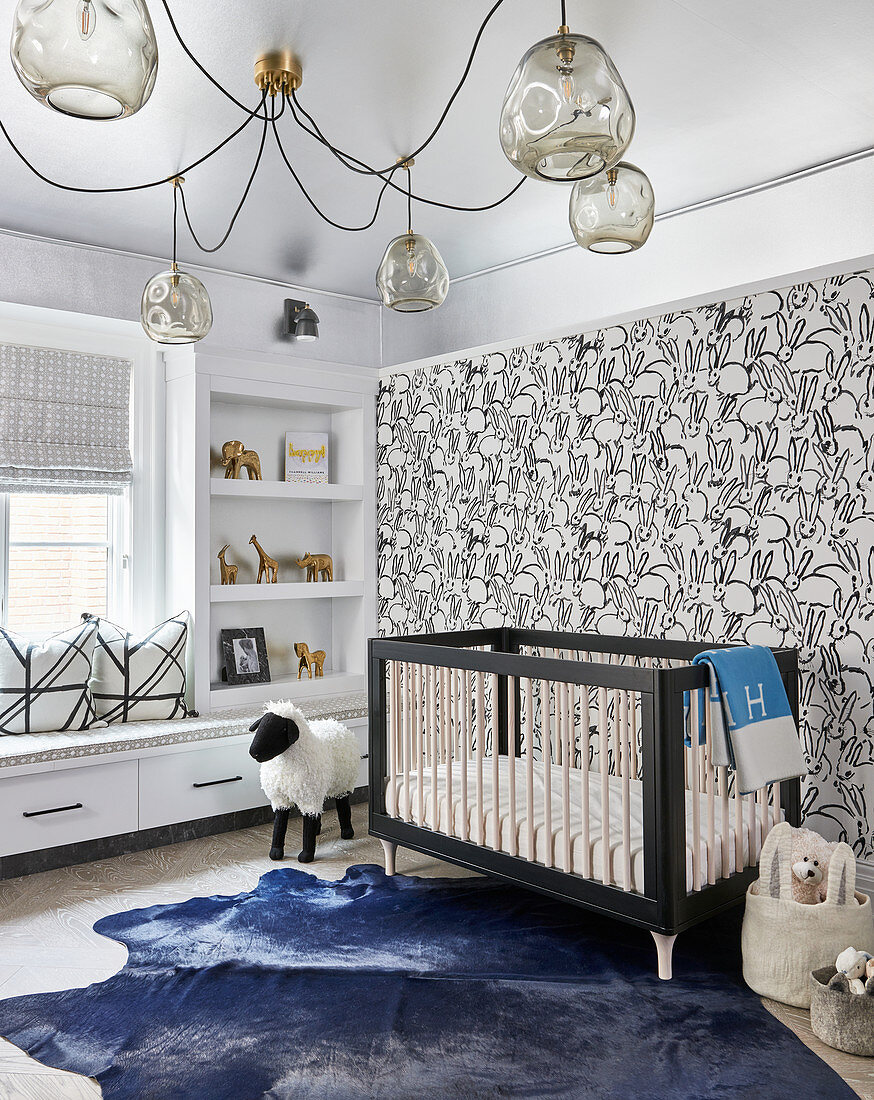 Kinderzimmer mit grafischer Kaninchen-Tapete, blauem Fellteppich, Gitterbett und Glaskugel-Kronleuchter