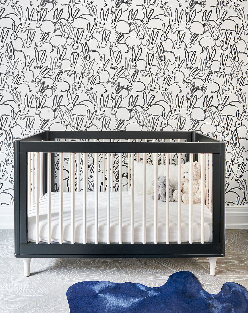 Gitterbett vor Kaninchen-Tapete und blauem Fellteppich im Kinderzimmer