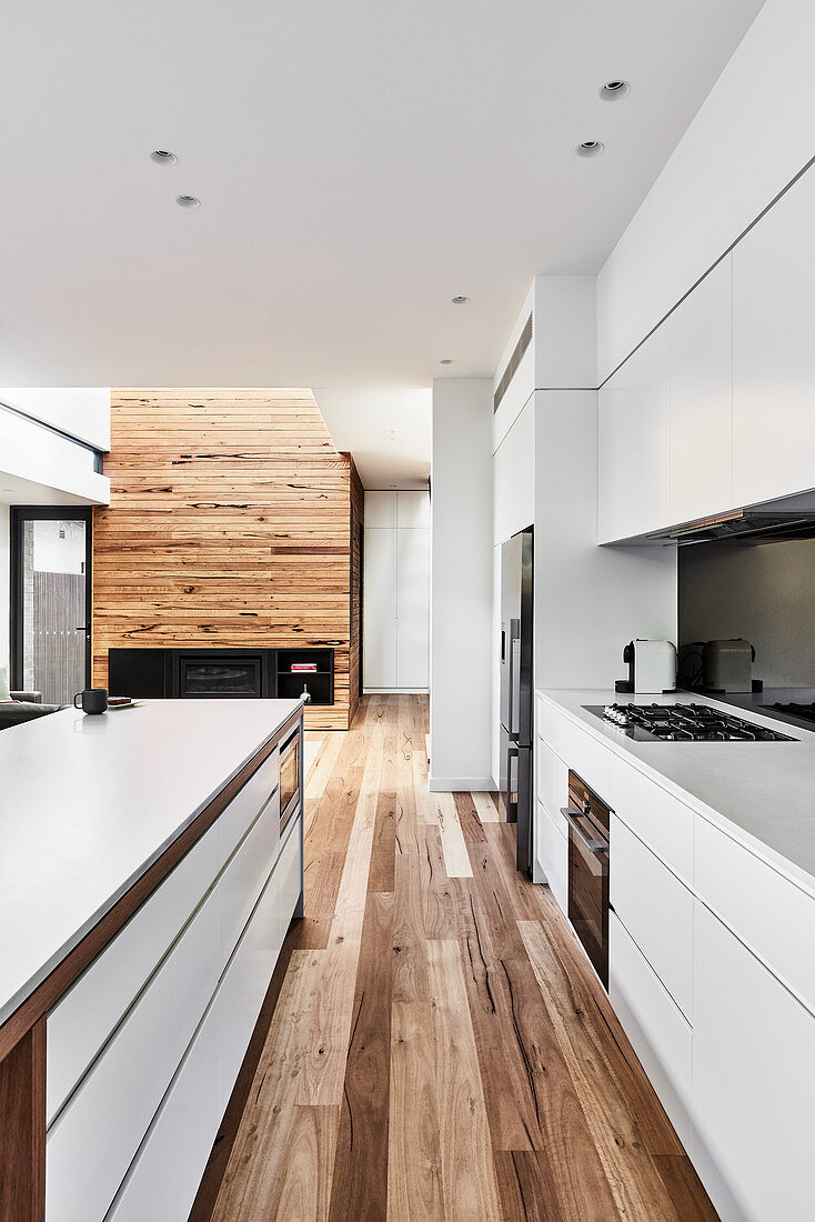 Modern open-plan kitchen in white in interior with wooden floor
