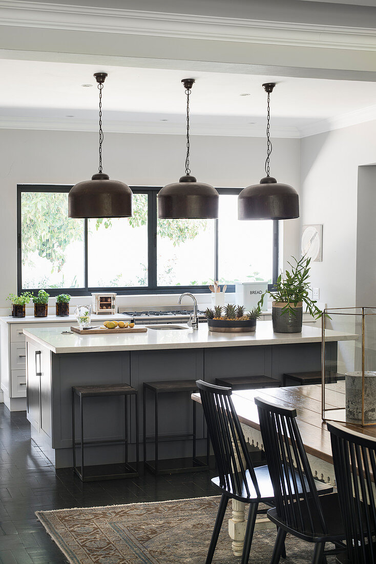 Island counter, industrial-style pendant lamps and dining area in open-plan kitchen