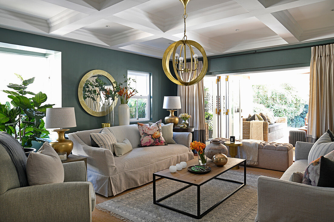 Pale upholstered furniture, coffee table, gilt pendant lamps and grey-green walls in living room