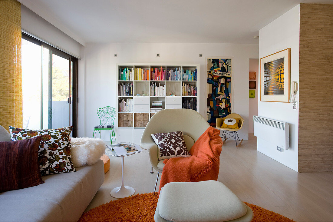 Offener Wohnraum mit Sofa, Designerstühlen, Regal und orangefarbenen Akzenten