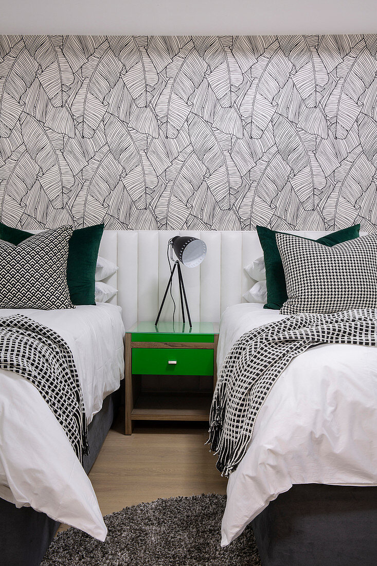 Grüner Nachttisch zwischen zwei Einzelbetten mit durchgehendem Bettkopfteil im Schlafzimmer