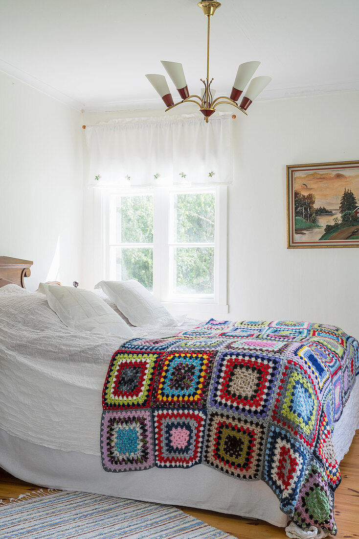 Multicoloured, crocheted granny-square blanket on double bed in vintage-style bedroom