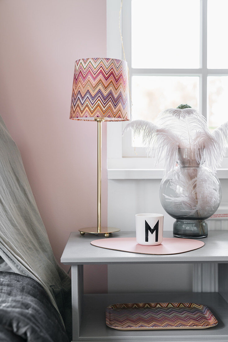 Table lamp with zigzag-patterned lampshade, feathers and mug with letter M