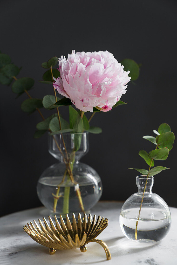 Peony and eucalyptus in small vases next to golden dish