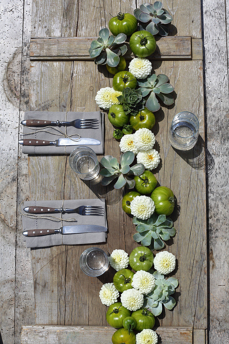 Girlande aus weißen Pompondahlien, grünen Tomaten und Hauswurz auf rustikalem Tisch
