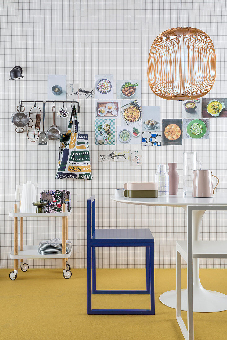 Tapete mit Karoheft-Muster in der Küche, Küchenutensilien an der Wand, Seriverwagen, Tisch und Stuhl