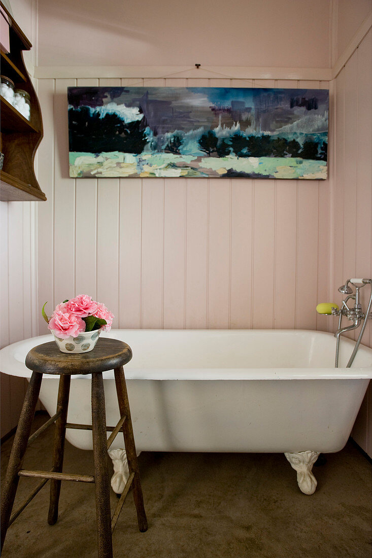 Vintage Badewanne, darüber Gemälde an holzverkleideter Wand im Bad, im Vordergrund Hocker mit Blumenschale