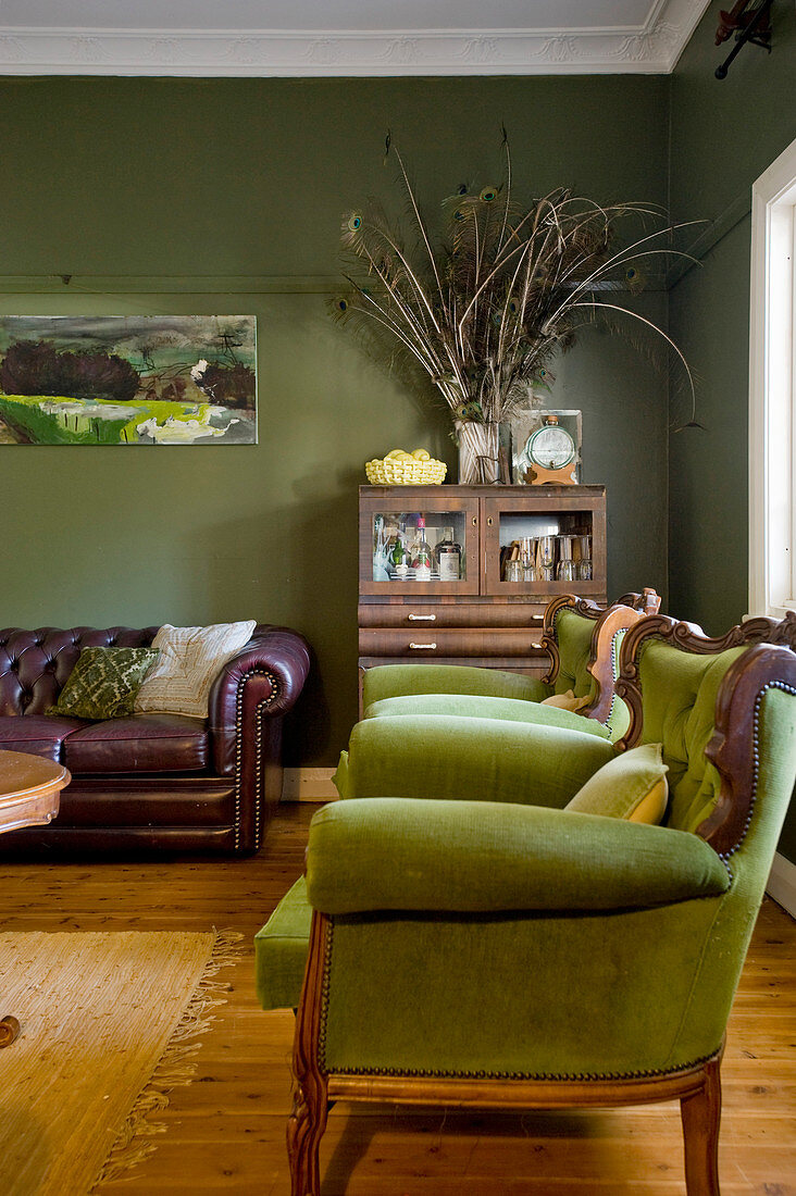 Grüne Polstersessel, halbhoher Schrank und Vintage Ledersofa im Wohnzimmer mit grünen Wänden