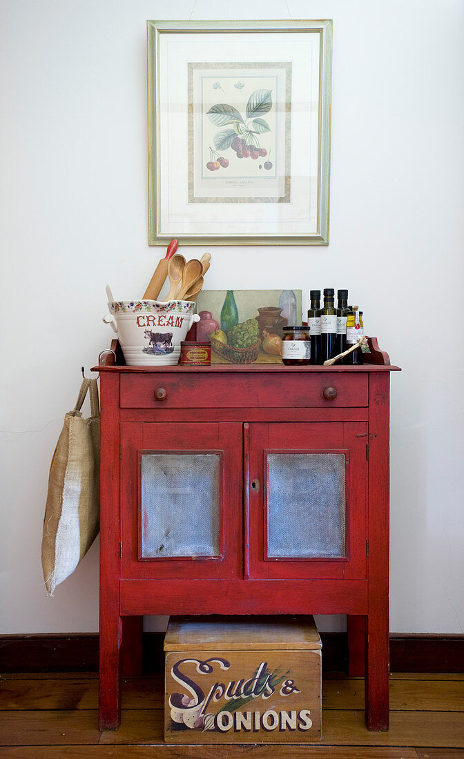 Bottles of olive oil, olives and kitchen utensils on red-painted cabinet