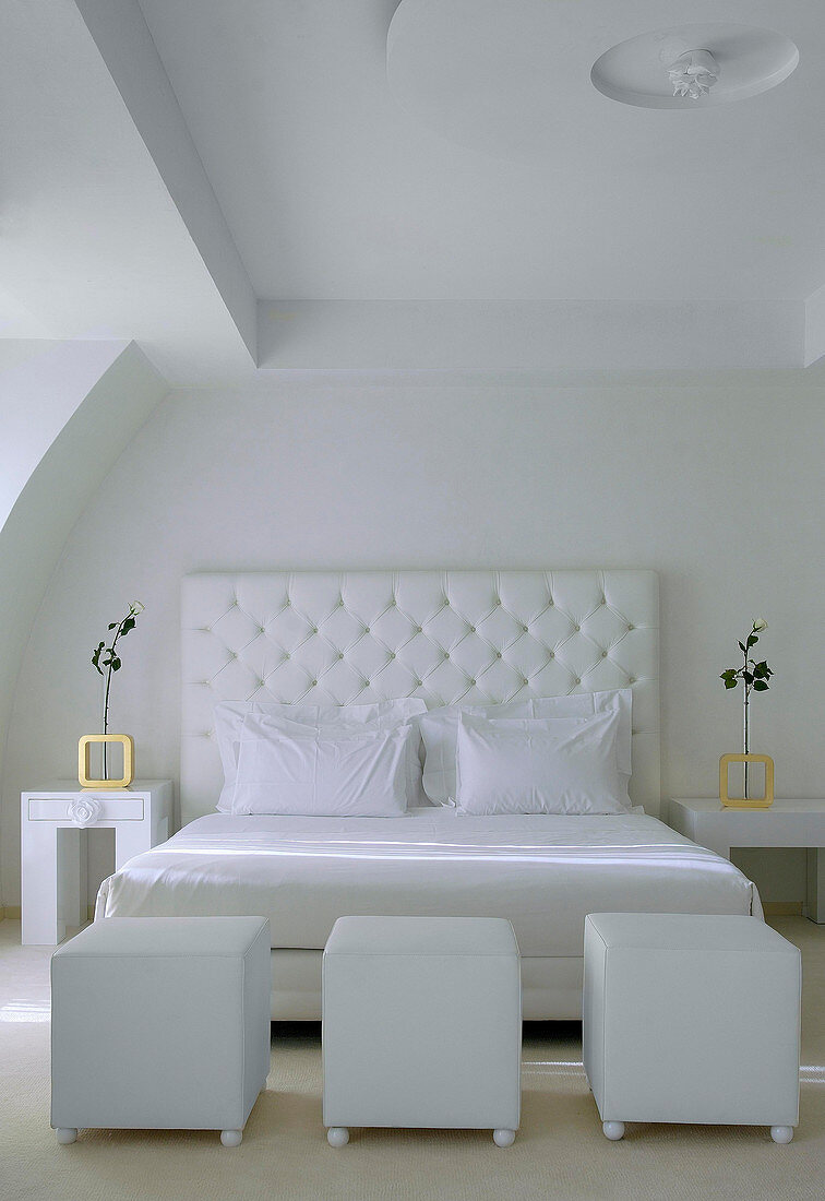 Doppelbett mit weißem Betthaupt und weiße Würfelhocker im Schlafzimmer