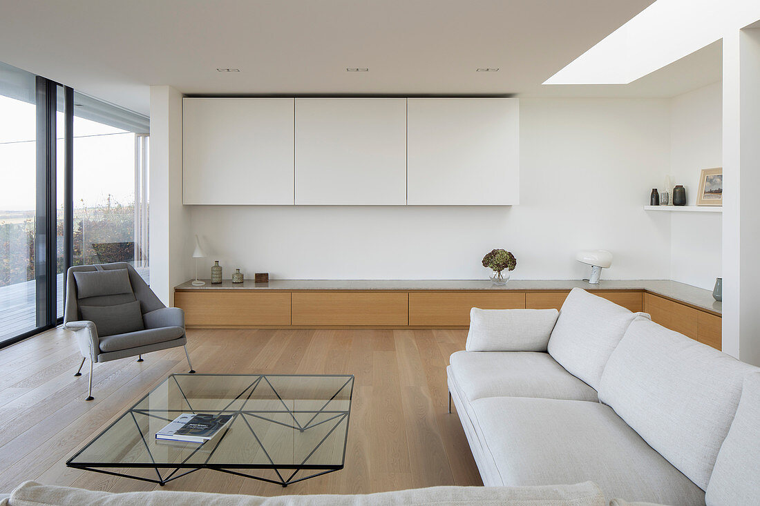 Pale sofa set, coffee table and low, custom sideboard in open-plan interior with glass wall