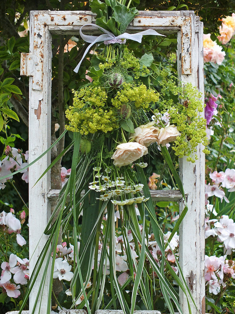 Summer bouquet hung in old window frame in front of rose bed