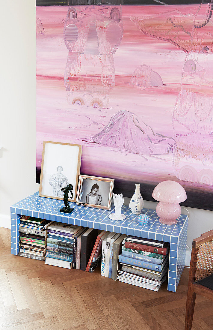 Books stacked below blue-tiled bench below pink painting