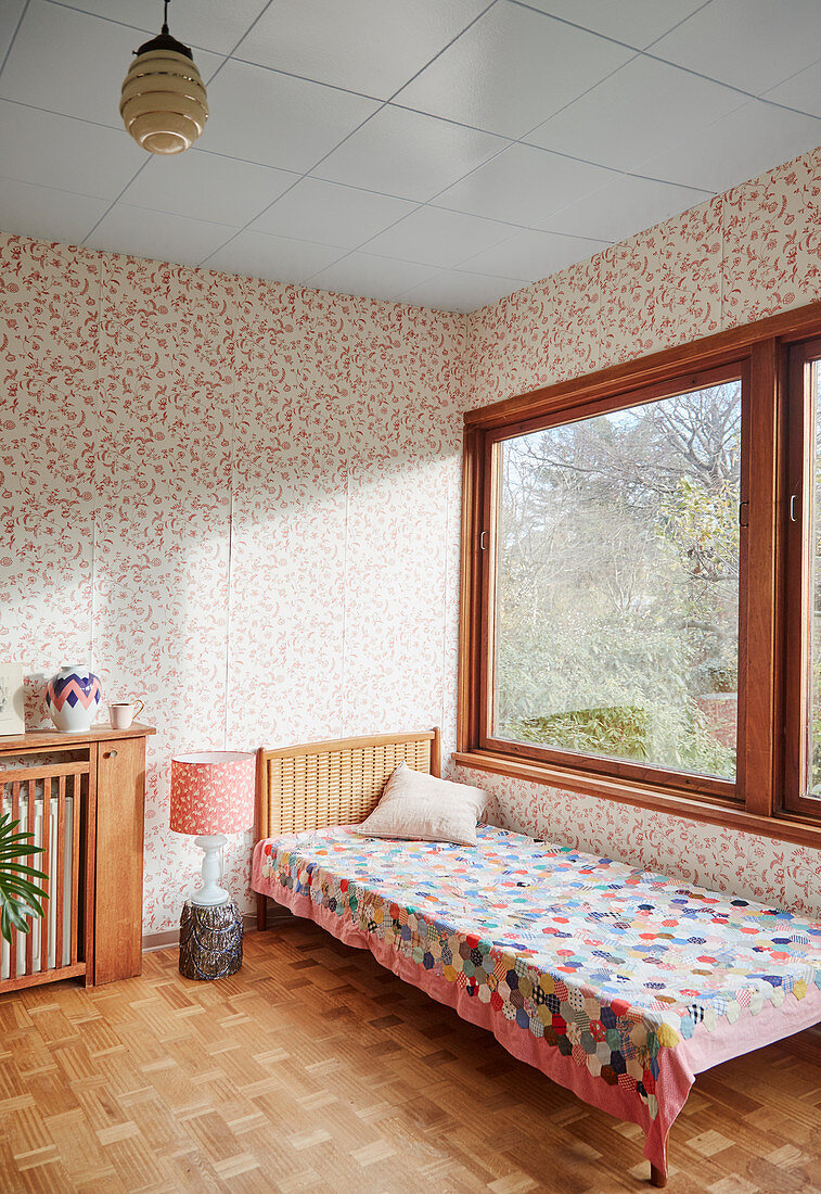 Bett mit Patchworkdecke im sonnigen Raum mit Vintage-Tapete