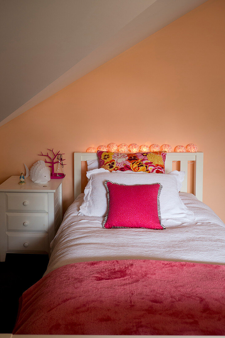Weißes Bett und Nachtkästchen im Dachzimmer mit apricotfarbener Wand