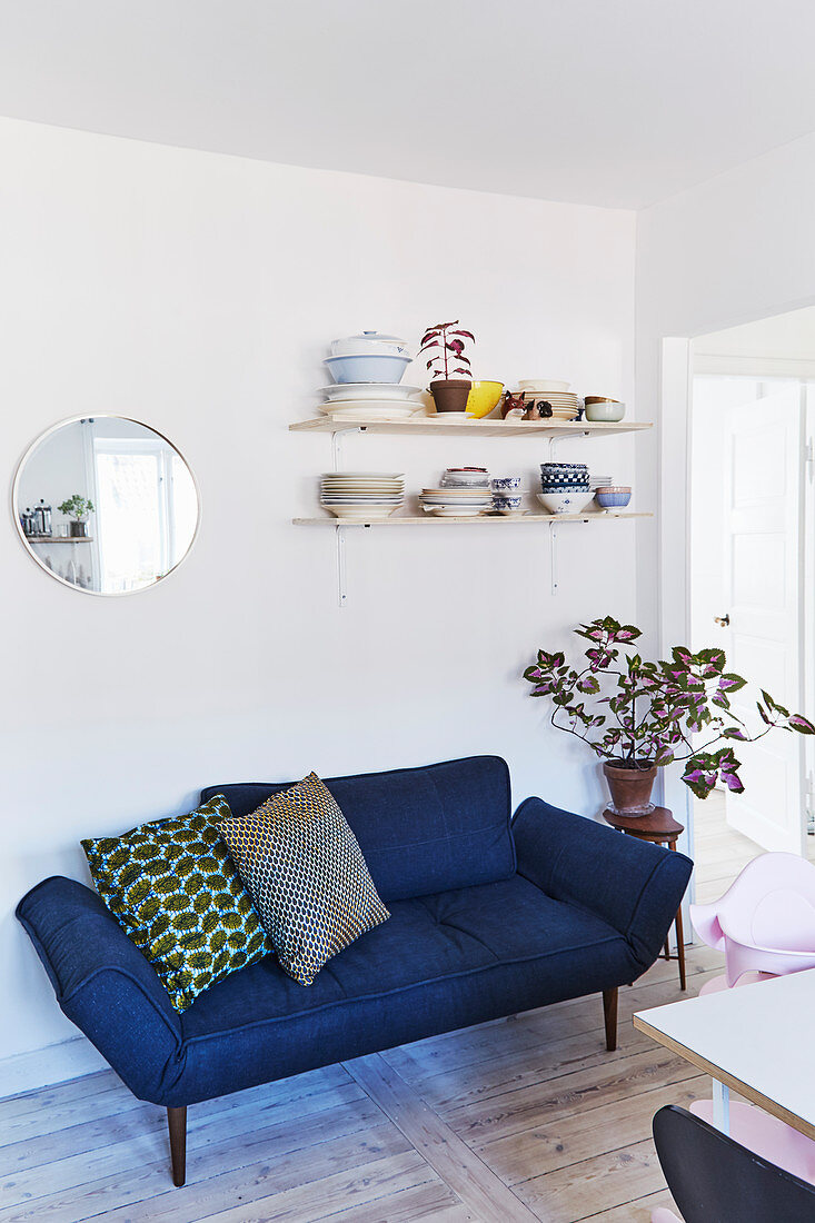 Contemporary blue sofa below shelves of crockery on wall in dining room