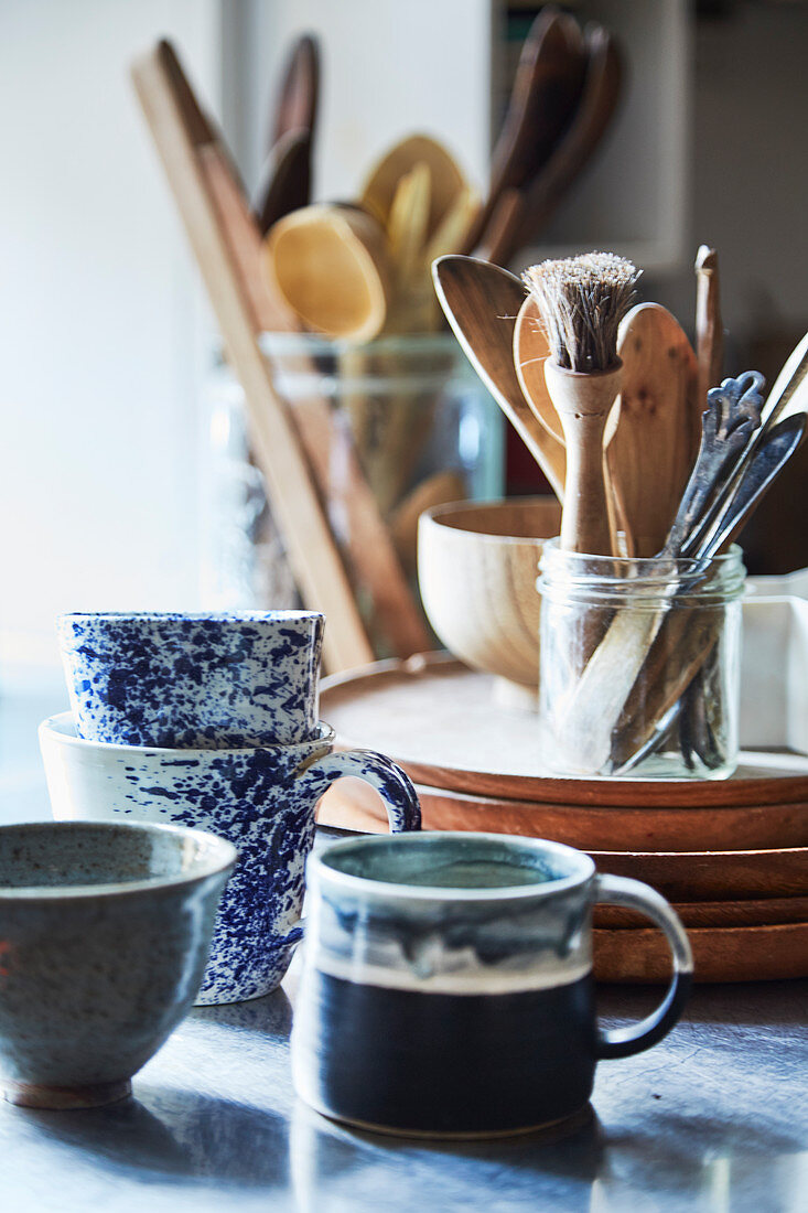 Keramiktassen, Holzteller und verschiedene Kochutensilien in Gläsern