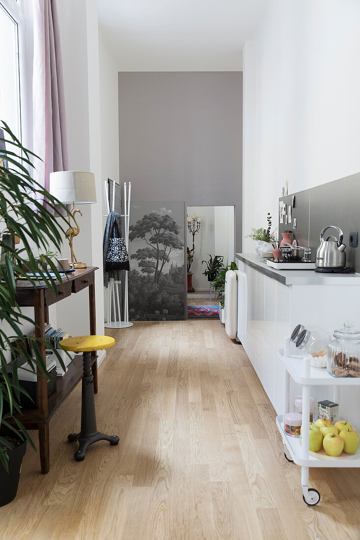Schmaler Wohnraum mit weißer Küchenzeile und Holzkonsolentisch mit Drehhocker fürs Homeoffice
