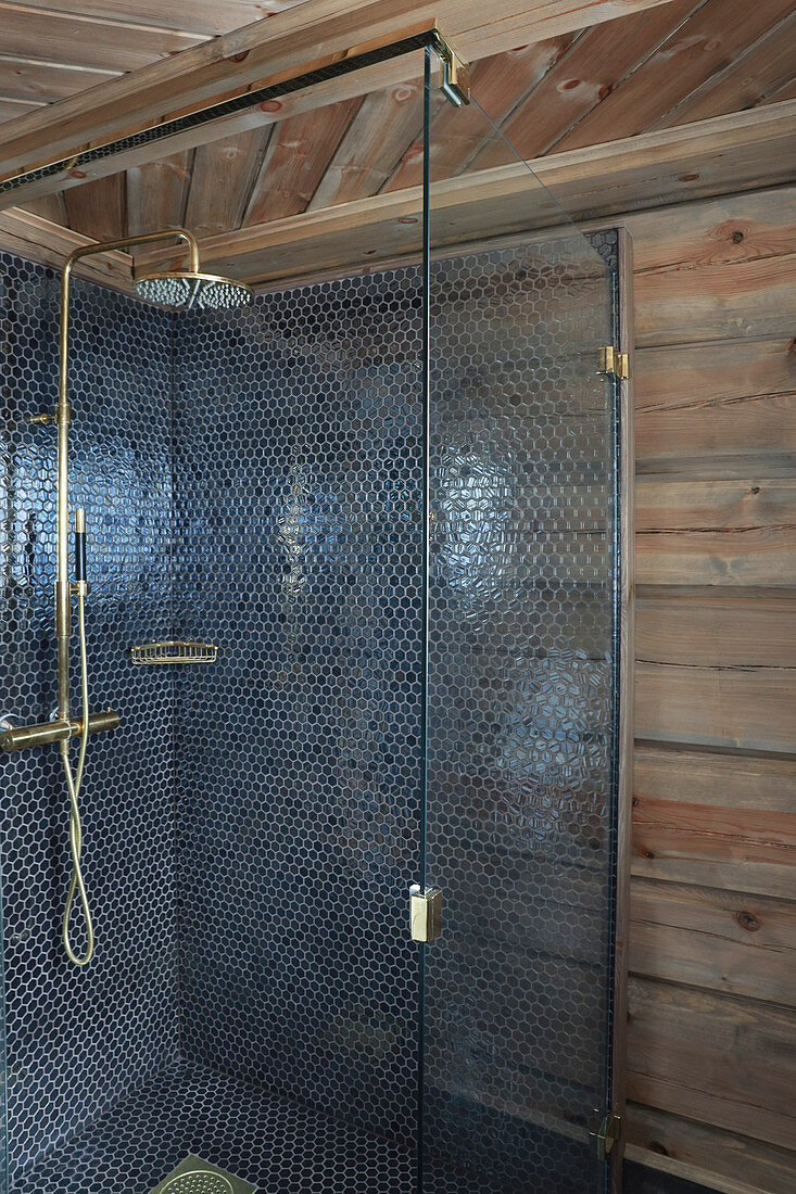 Blue mosaic tiles and golden shower fittings in shower cabin in log cabin