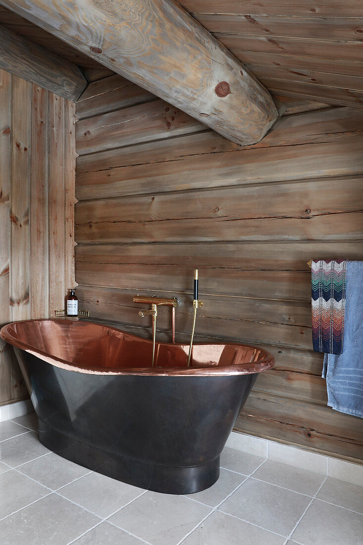 Free-standing copper bathtub in bathroom of log cabin