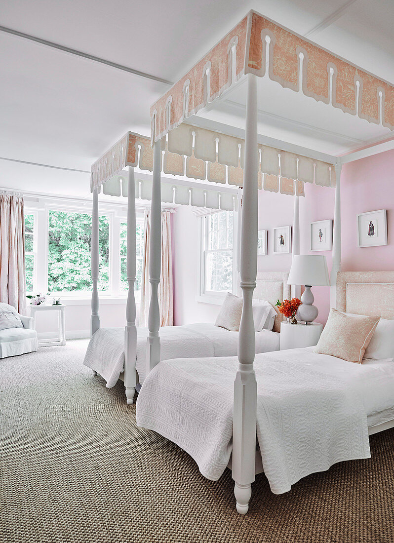Zwei weiße Pfostenbetten mit Schabracken in Schlafzimmer mit zartrosa Wänden und Vorhängen