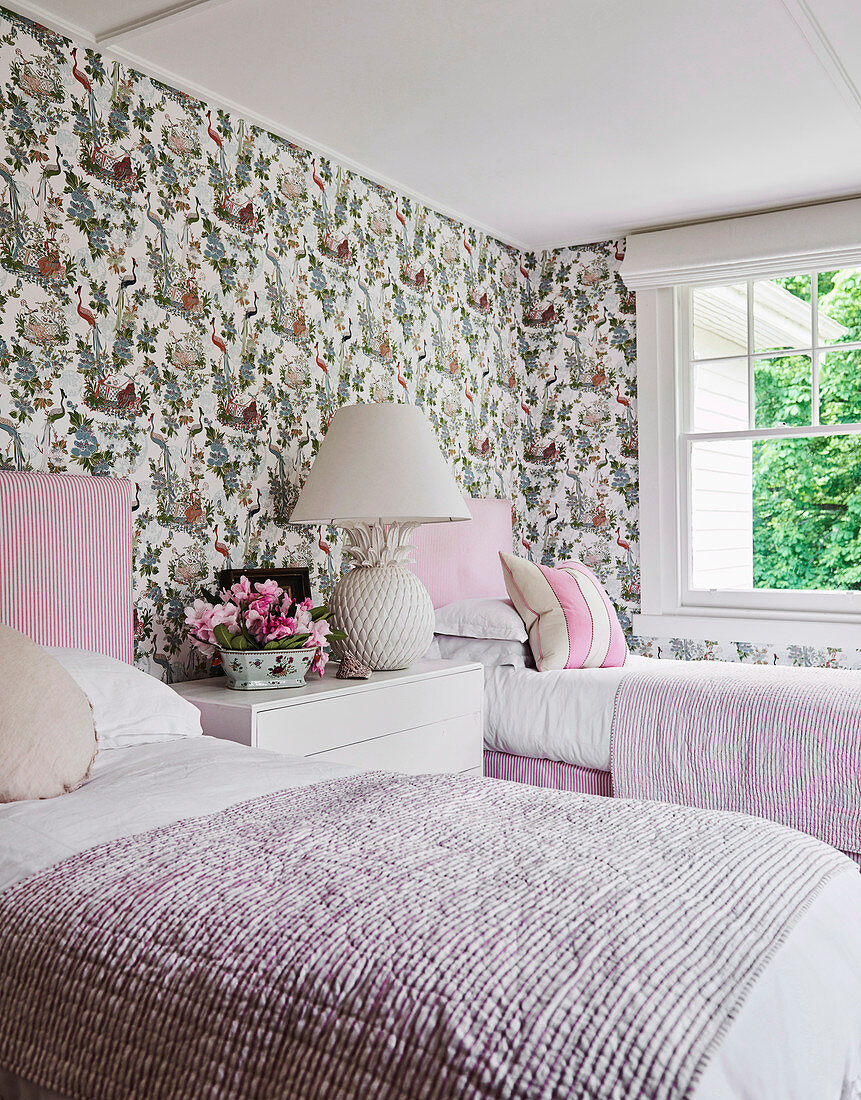 Two white and pink single beds against a wall with floral pattern wallpaper