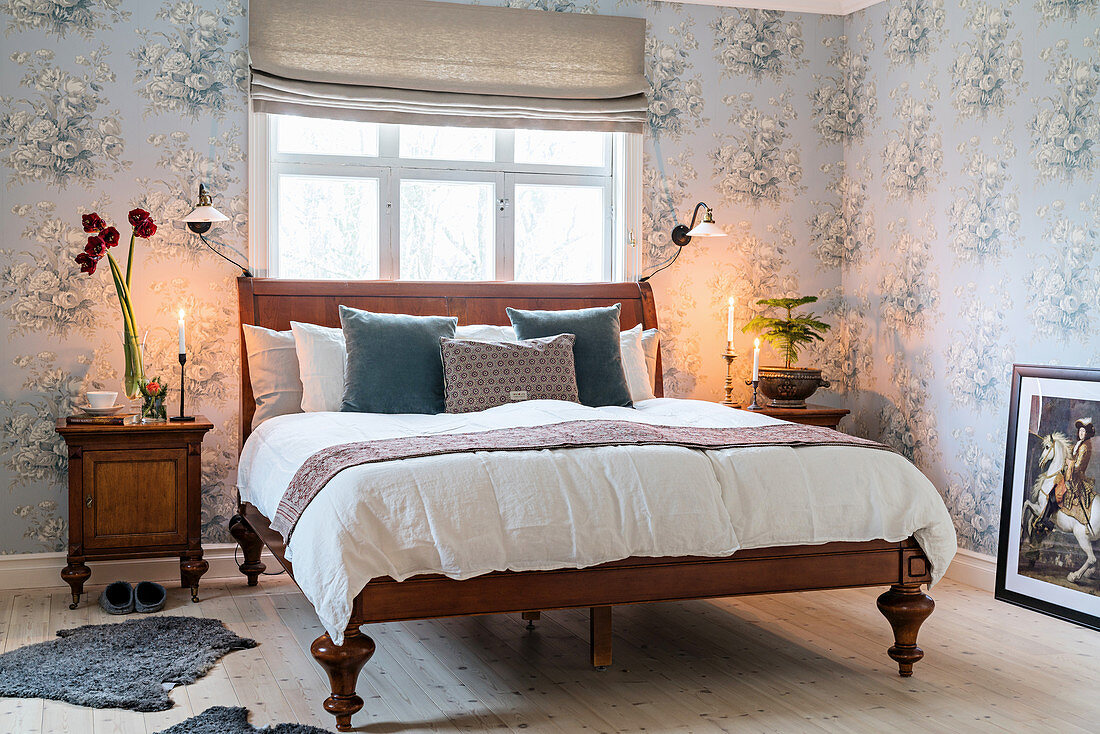 Antique wooden bed in bedroom with romantic, pale-blue floral wallpaper