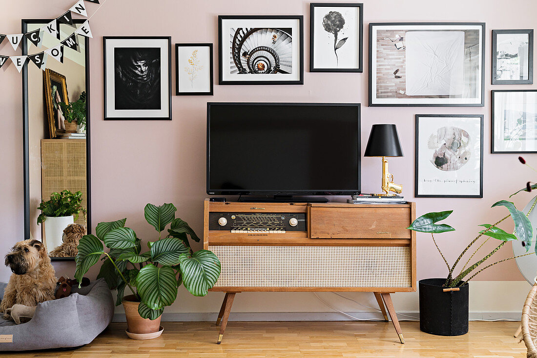 TV on top of retro radio below gallery of pictures on pink wall