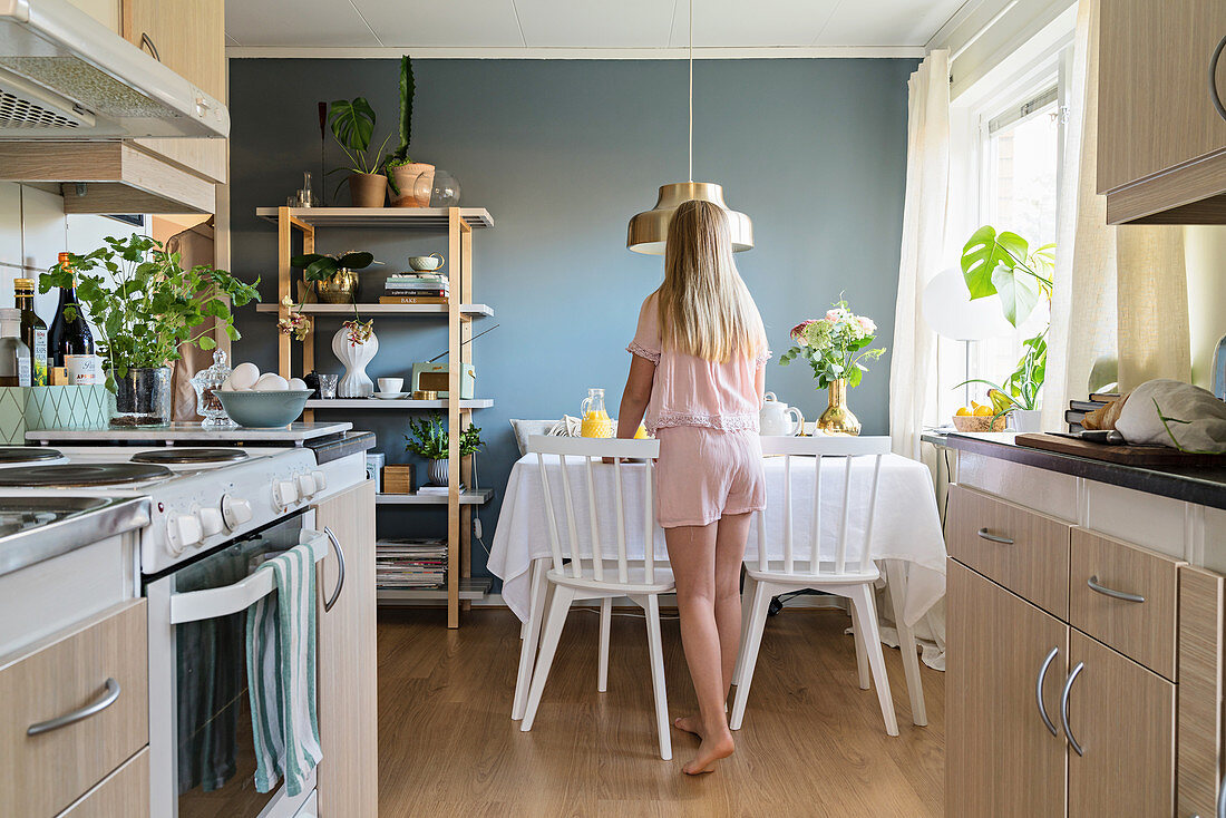Mädchen im Pyjama deckt den Frühstückstisch vor offener Küche