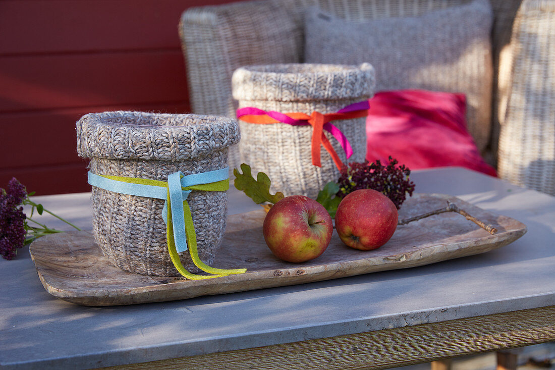 Candle lanterns with knitted covers and apples on wooden tray