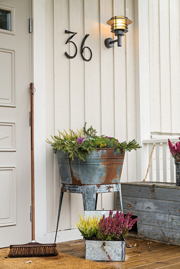 Plants in metal tub next to front door with house number and sconce lamp