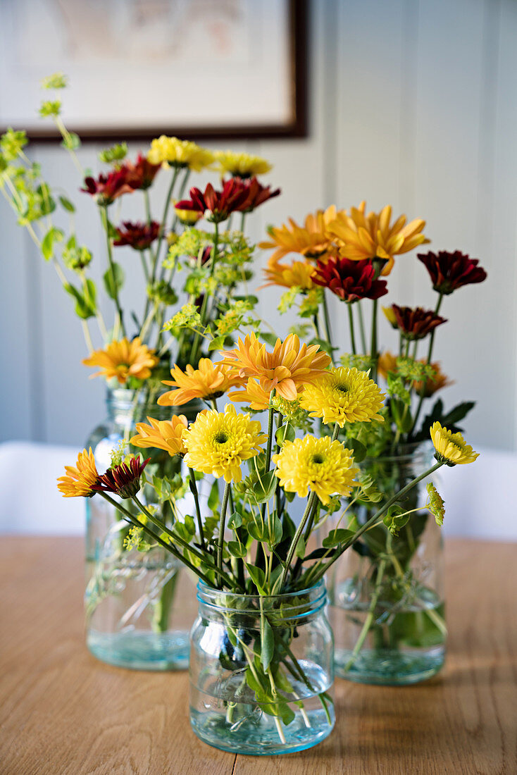 Flowers in shades of yellow and red in glass jars and bottle
