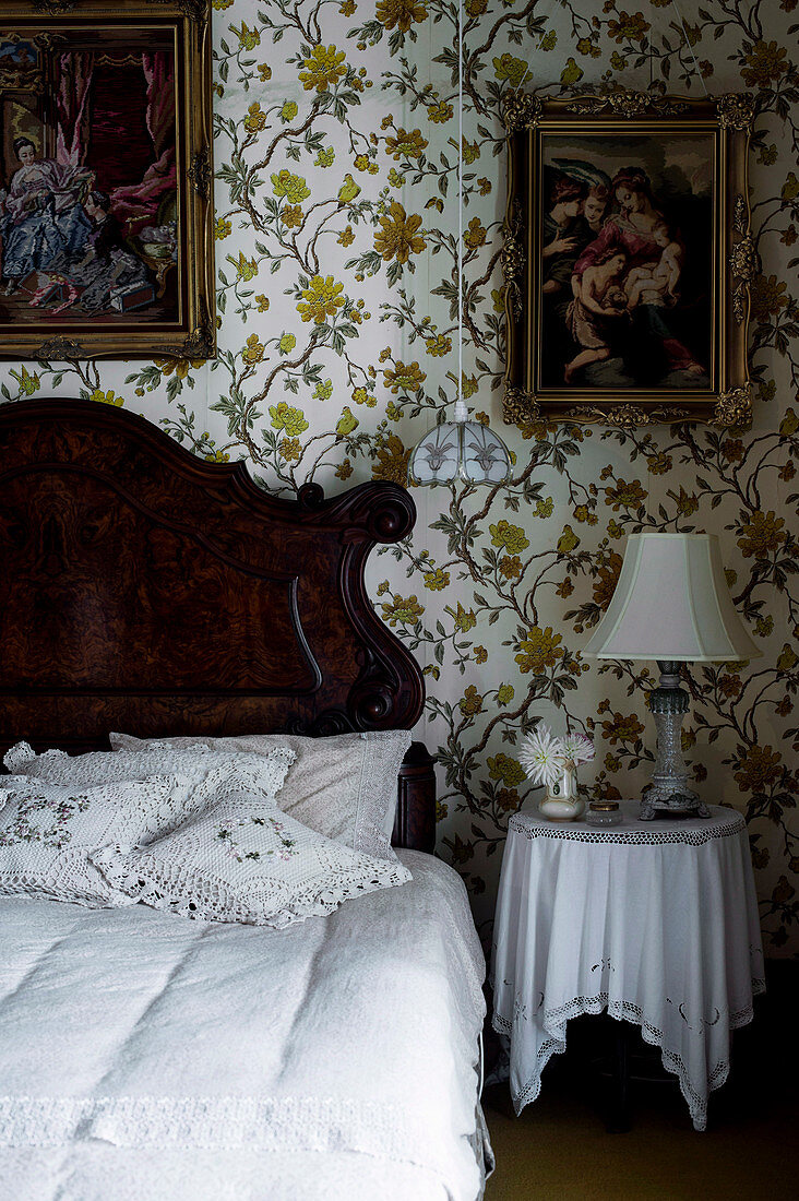 Rustikales Holzbett mit Kissen, Nachttisch und Gemälde an tapezierter Wand im Schlafzimmer