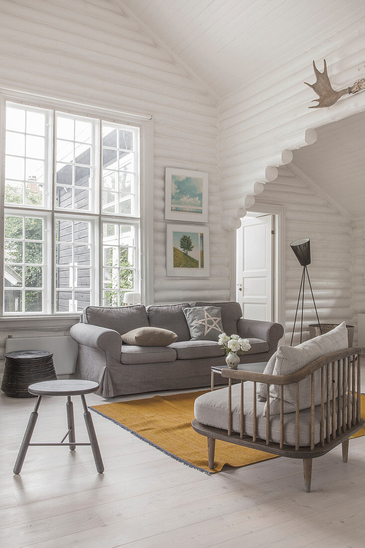 Sessel mit grauem Polster und passendes Sofa vor Fenster in weiß gestrichenem Blockhaus