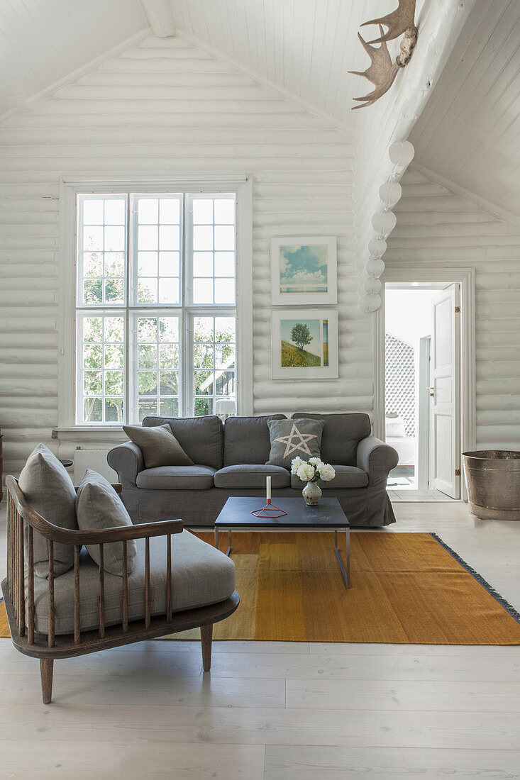 Sessel mit grauem Polster, passendes Sofa und Couchtisch in weiß gestrichenem Blockhaus