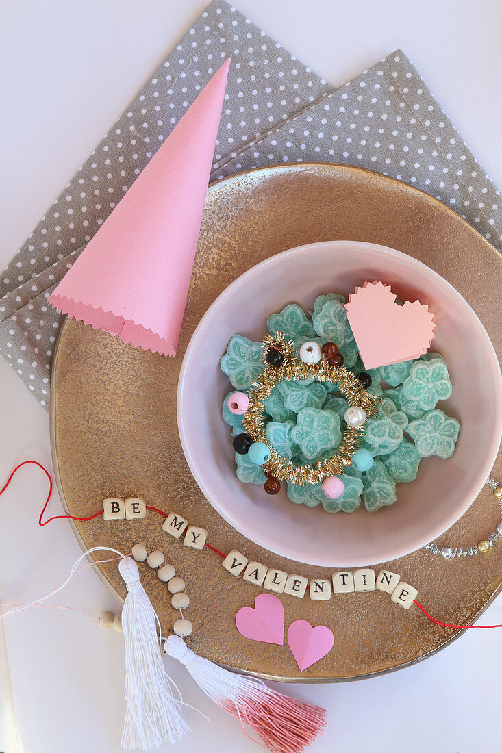 Arrangement of sweets, paper cone and string of lettered beads on plate
