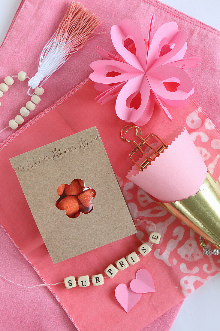 Romantisches Stillleben in Rosa mit Buchstabenkette und Bonbon-Tüte
