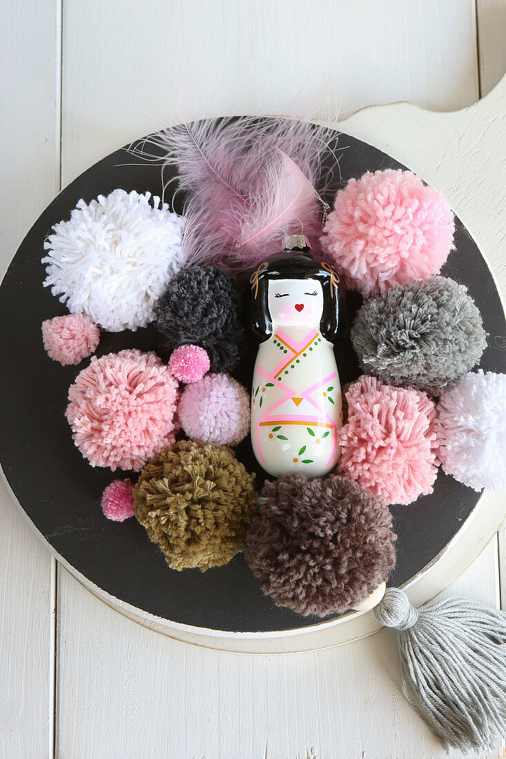 Geisha figurine and pompoms in pink and earthy tones on black plate