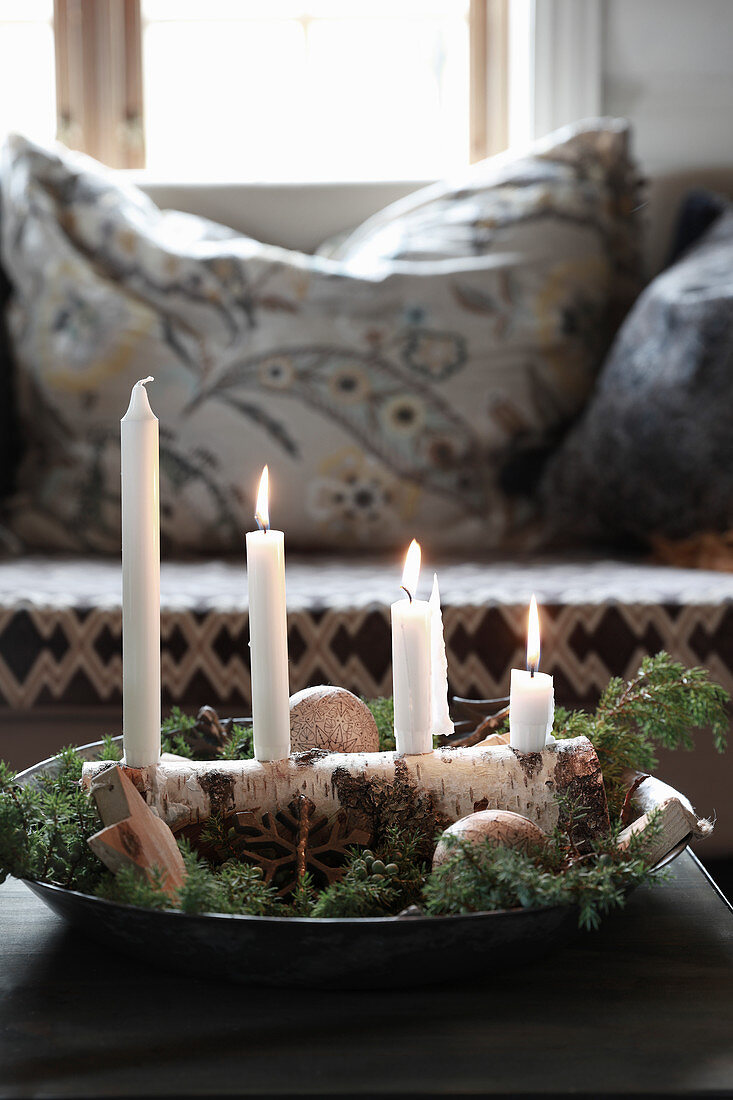 Vier Kerzen auf einem Stück Birkenast in der Schale als Adventskranz