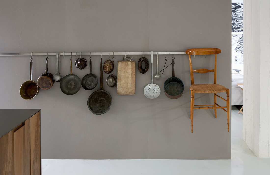 Kochgeschirrsammlung und filigraner Holzstuhl an grauer Wand