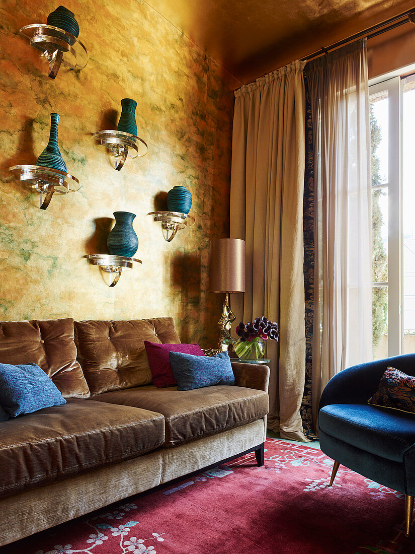 Consoles with turquoise vases on gold-colored wallpaper above an upholstered sofa